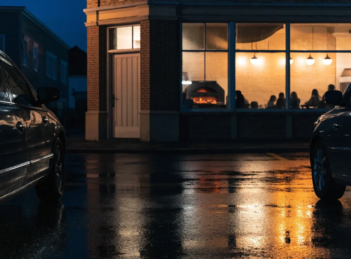 Lit pizzeria storefront seen from wet parking lot at night